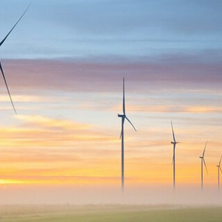wind turbines producing wind energy in front of a sunset