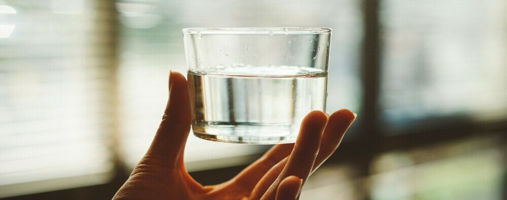 a woman's hand holding a glass of water for proper hydration